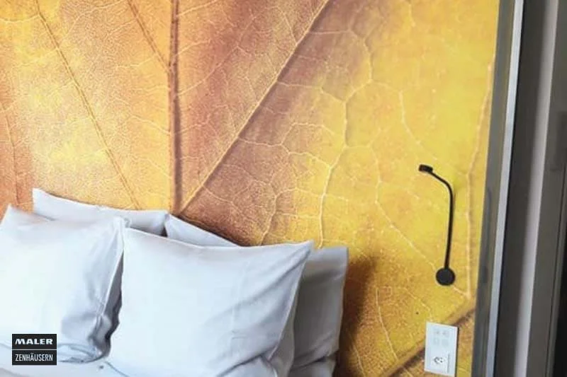 Foto eines Hotelzimmers mit Fokus auf die Wandtapete hinter dem Bett mit einem großen, goldgelben Blatt